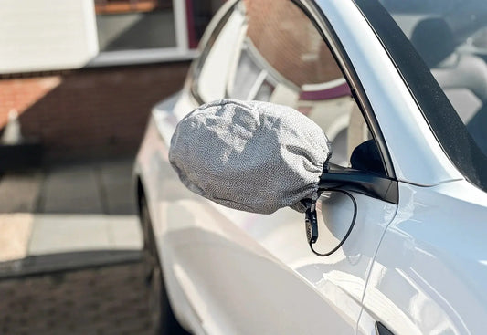 Auto met beschermhoezen over de buitenspiegels ter bescherming tegen spiegeldiefstal op een donkere woonstraat